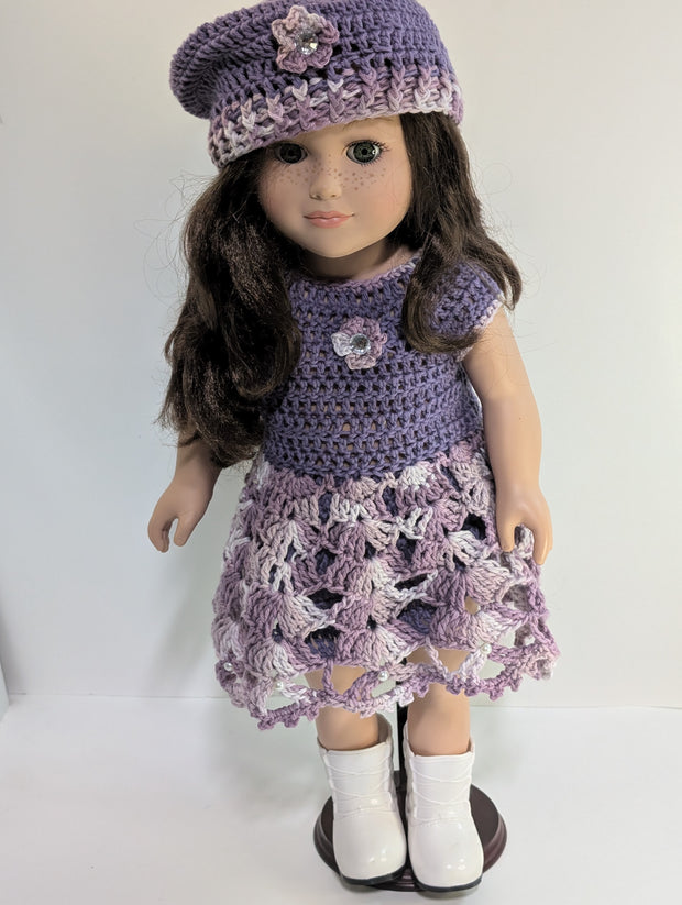 An elegantly displayed amigurumi doll from FashionableCrochet showcases the art of handmade crochet doll clothes, featuring a purple crocheted dress and matching beret adorned with floral accents. Her long, dark hair and white boots complete her stylish look.