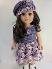 An elegantly displayed amigurumi doll from FashionableCrochet showcases the art of handmade crochet doll clothes, featuring a purple crocheted dress and matching beret adorned with floral accents. Her long, dark hair and white boots complete her stylish look.