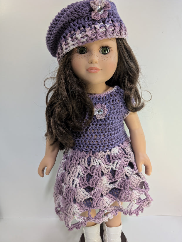 An elegantly displayed amigurumi doll from FashionableCrochet showcases the art of handmade crochet doll clothes, featuring a purple crocheted dress and matching beret adorned with floral accents. Her long, dark hair and white boots complete her stylish look.