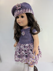 An elegantly displayed amigurumi doll from FashionableCrochet showcases the art of handmade crochet doll clothes, featuring a purple crocheted dress and matching beret adorned with floral accents. Her long, dark hair and white boots complete her stylish look.