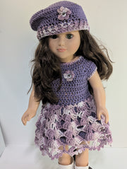 An elegantly displayed amigurumi doll from FashionableCrochet showcases the art of handmade crochet doll clothes, featuring a purple crocheted dress and matching beret adorned with floral accents. Her long, dark hair and white boots complete her stylish look.