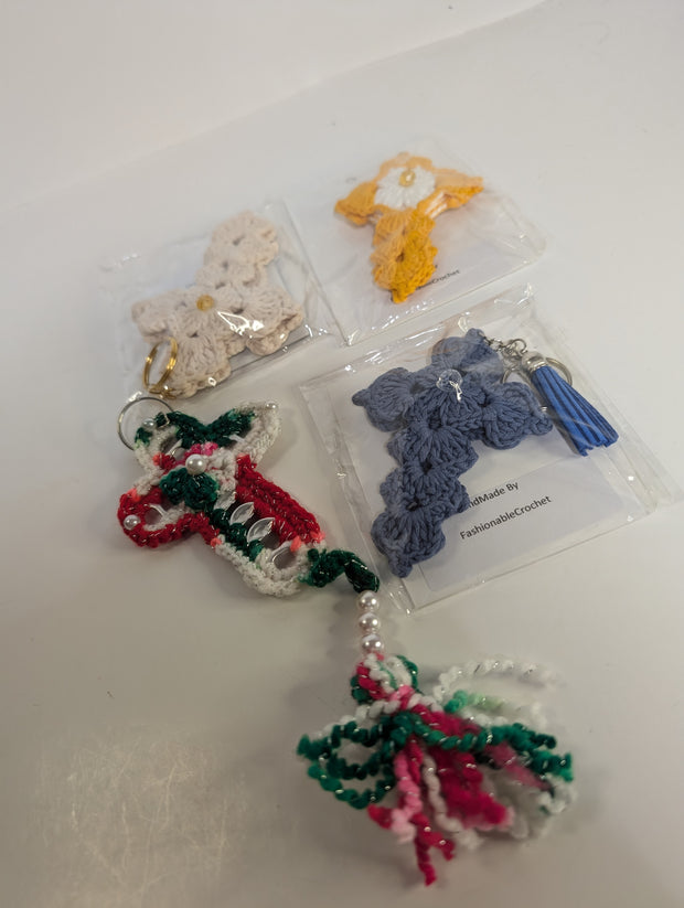 A variety of crochet keychains, featuring designs like a butterfly, candy cane, and the Handmade Crochet Cross Keychain – Spiritual Amigurumi Accessory by FashionableCrochet, are displayed on a table. Each piece is meticulously handcrafted and individually packaged.