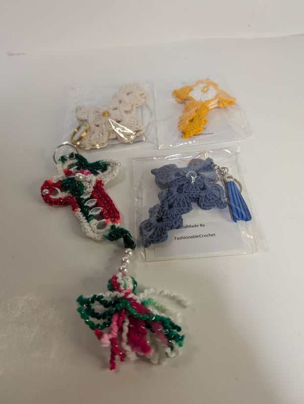 A variety of crochet keychains, featuring designs like a butterfly, candy cane, and the Handmade Crochet Cross Keychain – Spiritual Amigurumi Accessory by FashionableCrochet, are displayed on a table. Each piece is meticulously handcrafted and individually packaged.