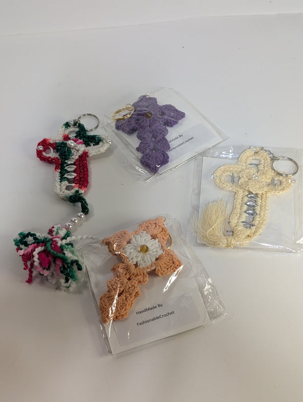 A variety of crochet keychains, featuring designs like a butterfly, candy cane, and the Handmade Crochet Cross Keychain – Spiritual Amigurumi Accessory by FashionableCrochet, are displayed on a table. Each piece is meticulously handcrafted and individually packaged.