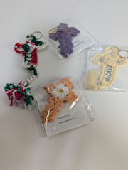 A variety of crochet keychains, featuring designs like a butterfly, candy cane, and the Handmade Crochet Cross Keychain – Spiritual Amigurumi Accessory by FashionableCrochet, are displayed on a table. Each piece is meticulously handcrafted and individually packaged.